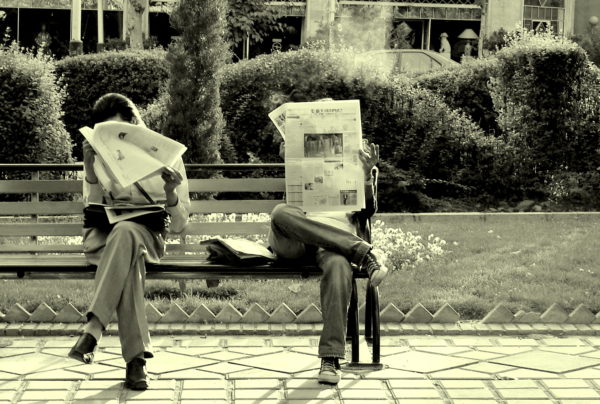 Old timey picture of people sitting on the  park bench reading newspapers