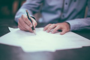 Man at desk writing by hand with a pen and paper.