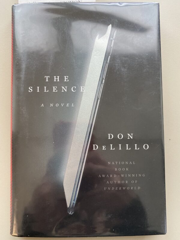 The front cover of The Silence featuring an image of a silent phone and a phone reflected in the cellophane cover photographing the cover.