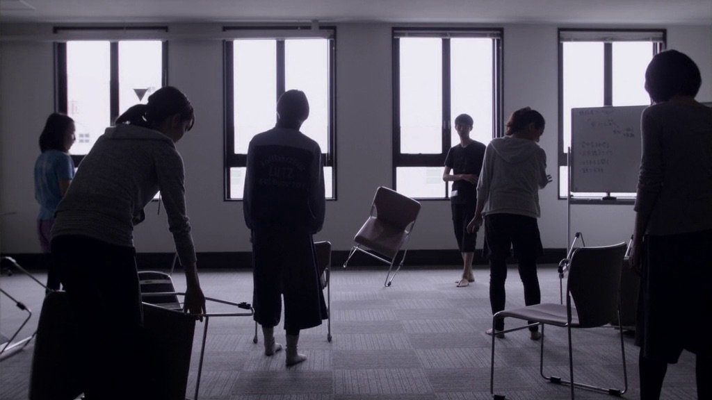 A group of people trying to balance chairs on a single leg, as seen in the Hamaguchi film "Happy Hour" (2015)