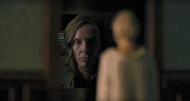 Still image from "Hereditary" of the character Annie in the background of a miniature figure.